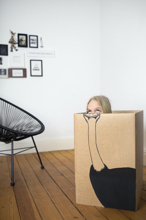 Girl inside a cardboard box painted with an ostrich