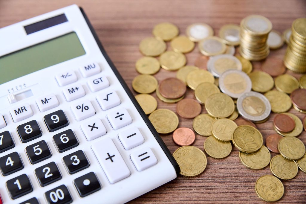 Wooden table with a glass jar containing coins and a calculator situated on top