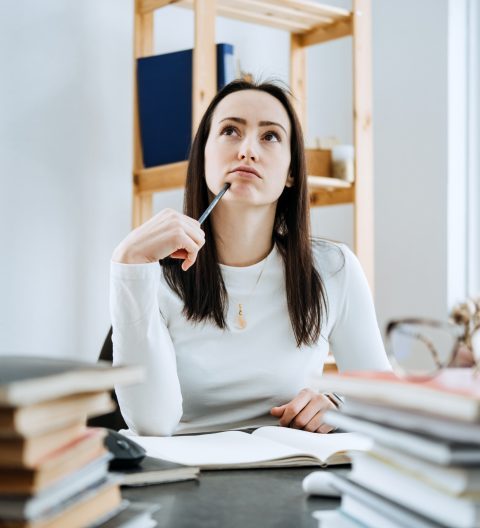 Woman considering a loan with many books and notepads on the background of laptop and calculator.